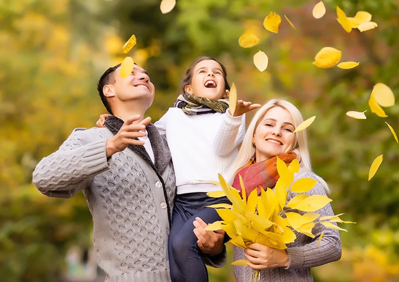 Family of three enjoying autumn leaves outdoors