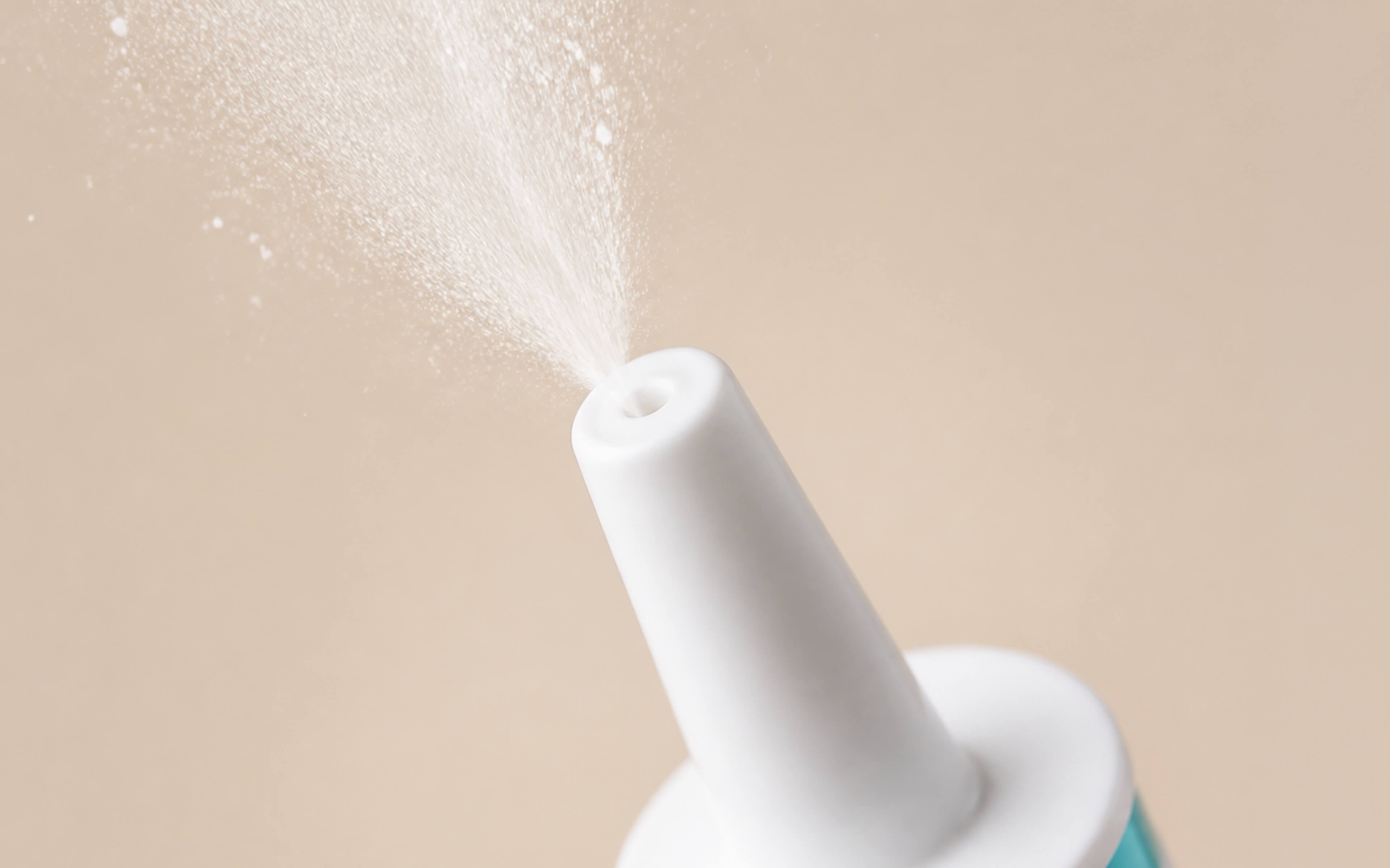 Close-up of a NOWONDER Nasal cleanser spray nozzle emitting a fine mist against a warm beige background.